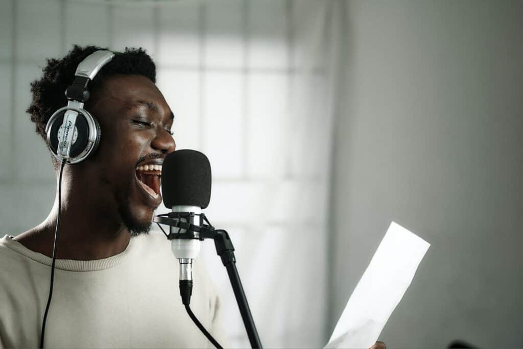 Gut gelaunter schwarzer Sprecher mit Kopfhörern vor einem Mikro, Emotionen erwecken durch gute Sprechertexte (Foto: Emmanuel Ikwuegbu)